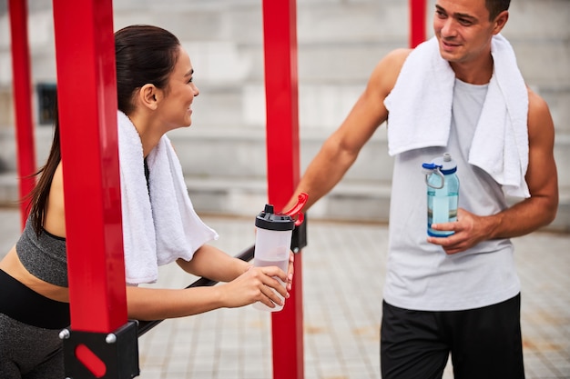 Hombre atlético sonriente está hablando con una mujer delgada después de entrenar en bares y agua potable