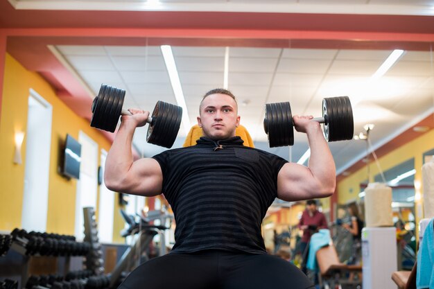 Foto el hombre atlético está sosteniendo la barra sobre la cabeza en el gimnasio.