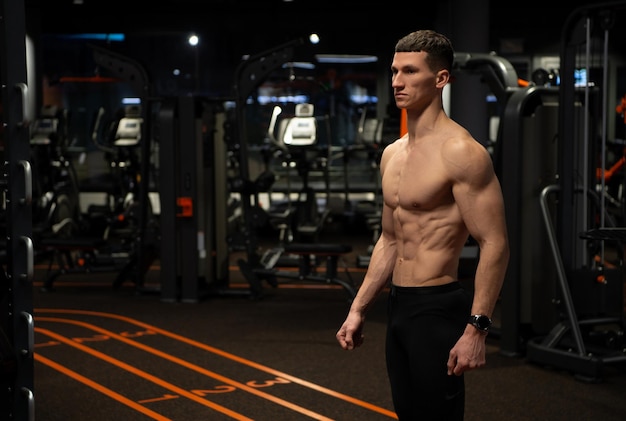 Hombre atlético con torso musculoso de pie en el gimnasio, deportista.