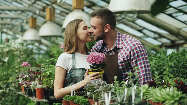 Un hombre atractivo abraza y besa a su esposa sosteniendo una flor y sonríe juntos a la cámara