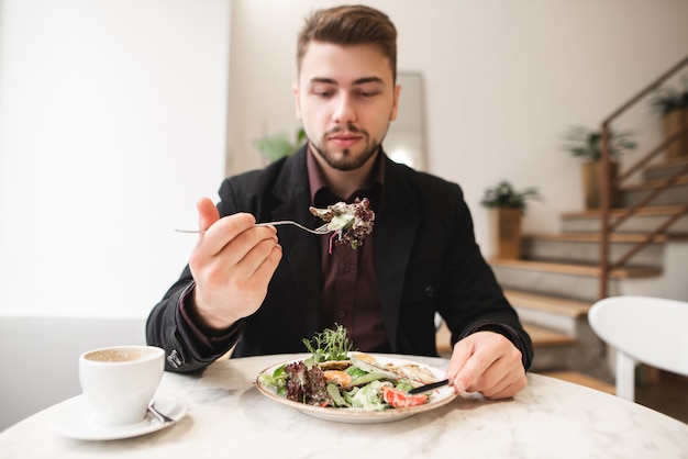 Hombre atractivo con barba comiendo una ensalada de dieta en un acogedor restaurante. El hombre tomó la ensalada verde en el tenedor