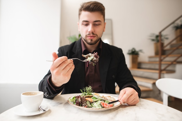 Hombre atractivo con barba comiendo una ensalada de dieta en un acogedor restaurante. El hombre tomó la ensalada verde en el tenedor