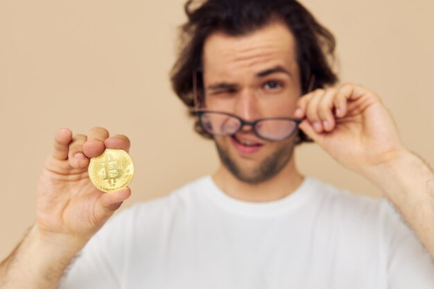 Hombre atractivo en una camiseta blanca con fondo beige de criptomoneda Bitcoin