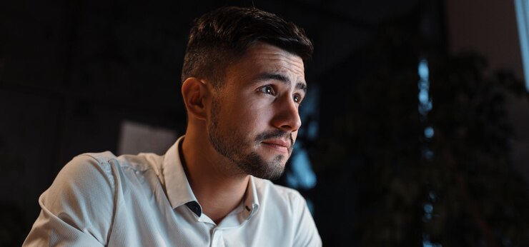 Un hombre atractivo concentrado en su trabajo mira su computadora en su oficina por la noche