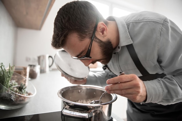 Hombre atractivo degustando comida de una sartén de pie en la cocina