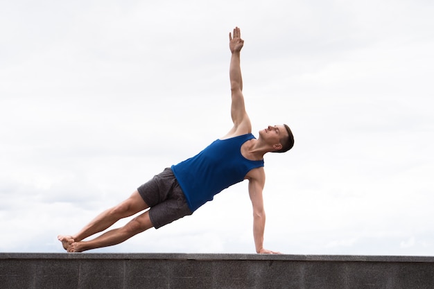 Hombre atractivo haciendo yoga al aire libre en el fondo del cielo