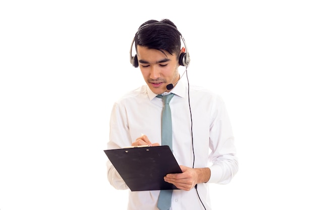 Hombre atractivo joven con cabello oscuro en camisa blanca con corbata usando auriculares y sosteniendo una carpeta