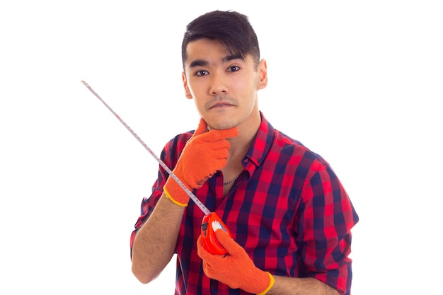 Hombre atractivo joven con cabello oscuro en camisa a cuadros roja con guantes naranjas sosteniendo una cinta métrica