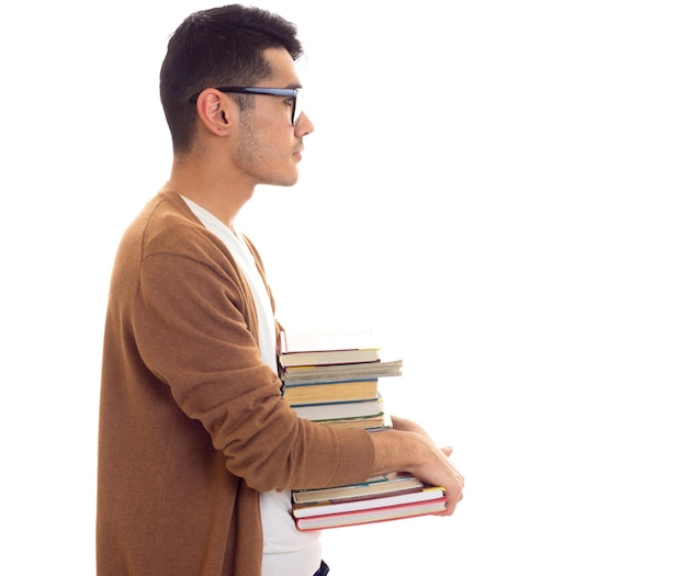 Hombre atractivo joven en cárdigan marrón de camiseta blanca con gafas negras sosteniendo una pila de libros