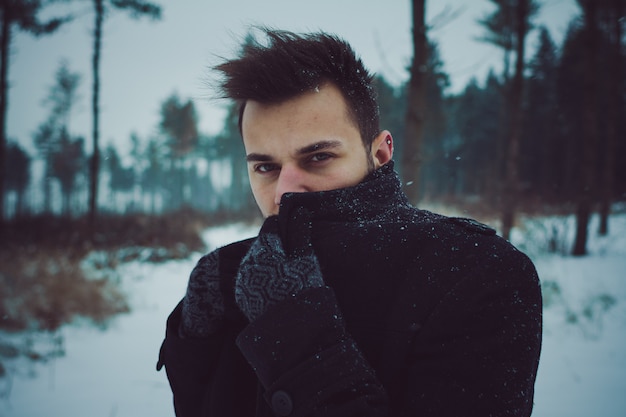 Hombre atractivo joven que abraza la nieve en invierno. Retrato de primer plano