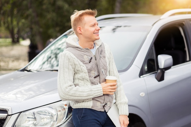 Hombre atractivo joven con taza de café de papel en el coche