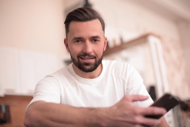 Hombre atractivo leyendo un SMS mientras está sentado y en la cocina