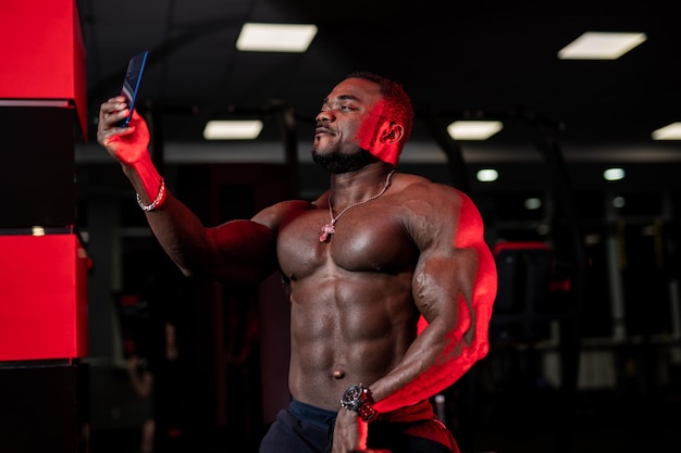 Hombre atractivo modelo de fitness afroamericano toma selfie sobre fondo de gimnasio. Foto para redes sociales. De cerca.
