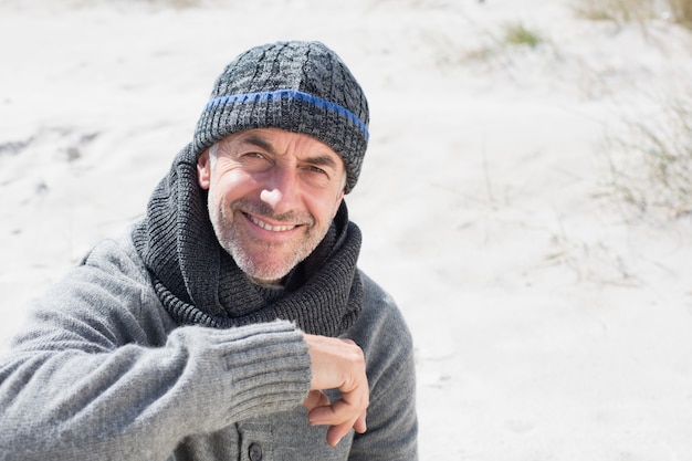 Hombre atractivo sonriendo en la playa con sombrero y bufanda