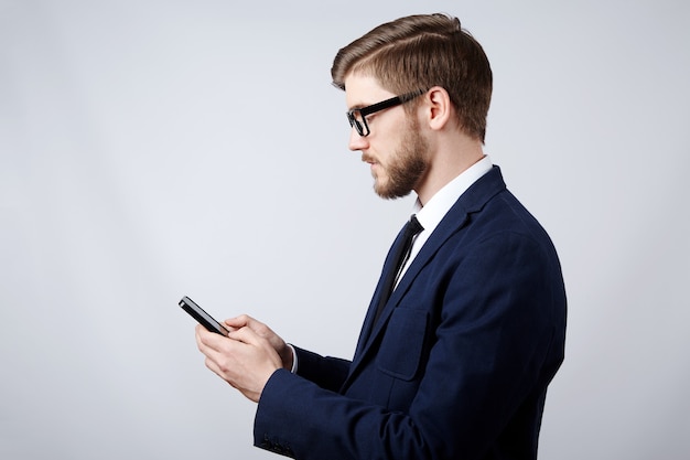 Hombre atractivo vestido con traje y gafas en el estudio con teléfono móvil