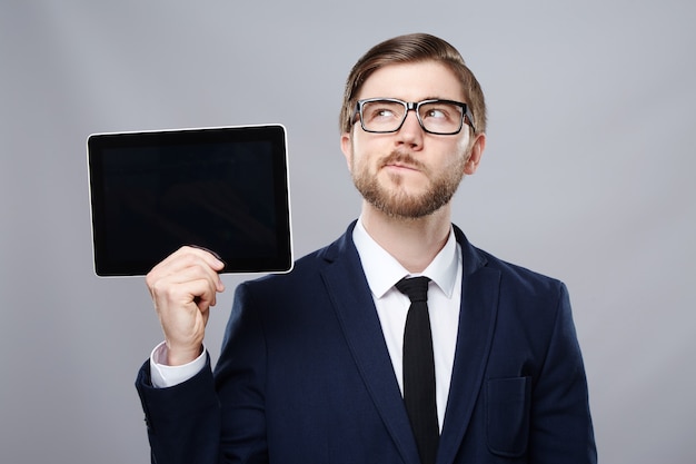 Hombre atractivo vestido con traje y gafas de pared sosteniendo una tableta y pensando, concepto de negocio, espacio de copia, retrato, maqueta.