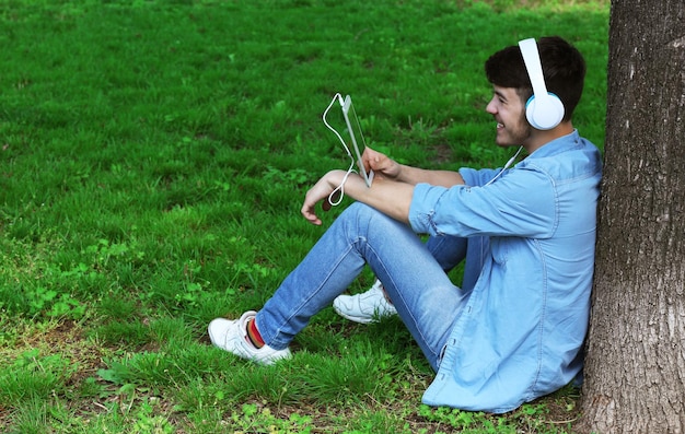 Hombre con auriculares descansando bajo un árbol en el parque