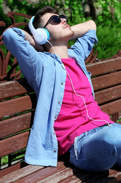 Foto hombre con auriculares descansando sobre un banco en el parque