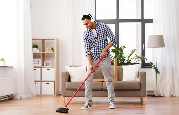 hombre con auriculares con escoba limpiando en casa