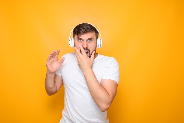 Un hombre con auriculares escuchando música se agarró la boca y demuestra horror.