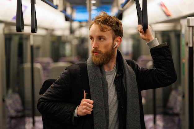 Un hombre con auriculares inalámbricos y una mochila está parado en un tren subterráneo