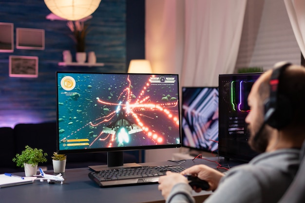 Hombre con auriculares y joystick en el espacio de transmisión de videojuegos en el estudio de juegos en casa. Hombre jugador profesional hablando con otros jugadores en línea para la competencia de juegos jugando en una computadora potente