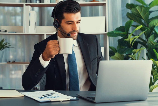 Foto un hombre con auriculares se sienta en un escritorio con una computadora portátil y una planta detrás de él.