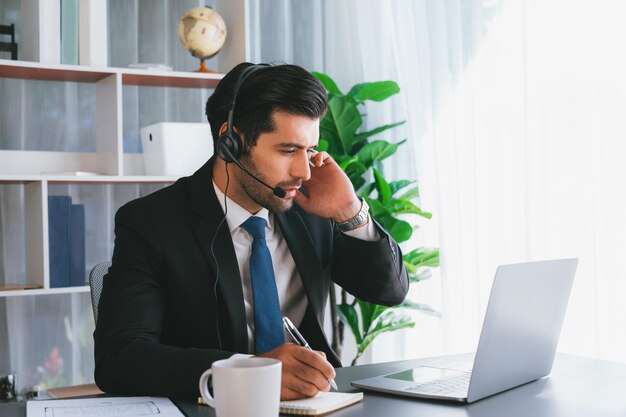 Un hombre con auriculares se sienta en un escritorio con una computadora portátil y una taza de café.