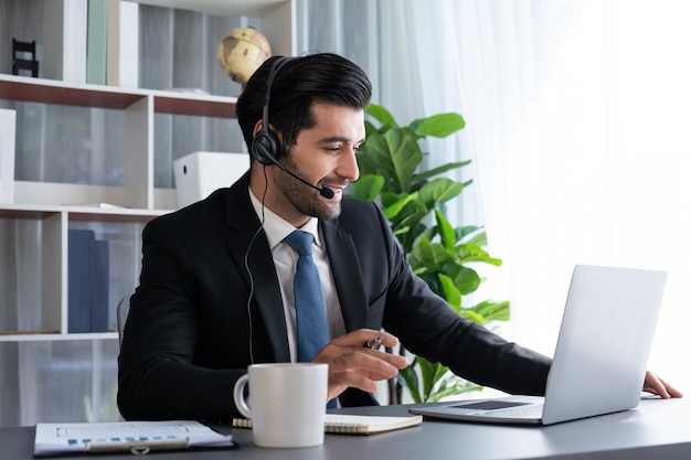Un hombre con auriculares se sienta en un escritorio con una computadora portátil y una taza de café.