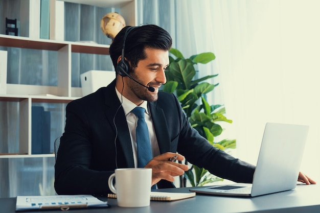 Un hombre con auriculares se sienta en un escritorio con una computadora portátil y una taza sobre la mesa.