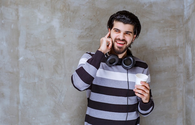 Hombre con auriculares sosteniendo una taza de agua blanca