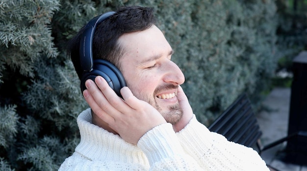 Un hombre con auriculares y un suéter blanco sonríe mientras usa un suéter blanco.