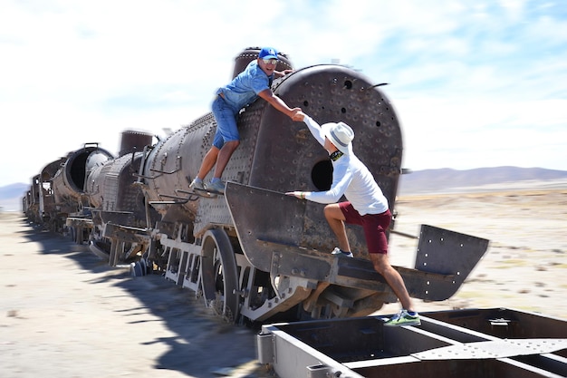 Foto hombre ayudando a un amigo mientras sube a un tren abandonado en el desierto
