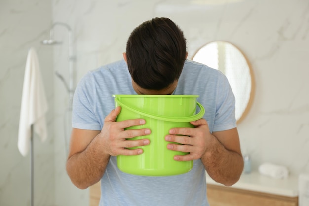 Foto hombre con balde que sufre de náuseas en el baño intoxicación alimentaria