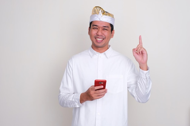 Hombre balinés sonriendo y señalando con el dedo mientras sostiene un teléfono móvil