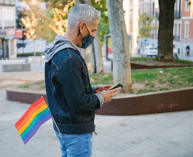 Hombre con bandera del arco iris con smartphone en ciudad