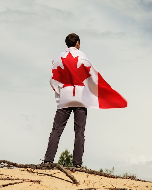 Un hombre con una bandera canadiense se encuentra en la arena, el cielo en el fondo.