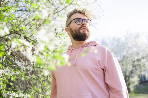 Foto hombre con barba y bigote en la cara sonriente cerca de las flores de sakura o el árbol de primavera en flor suave y