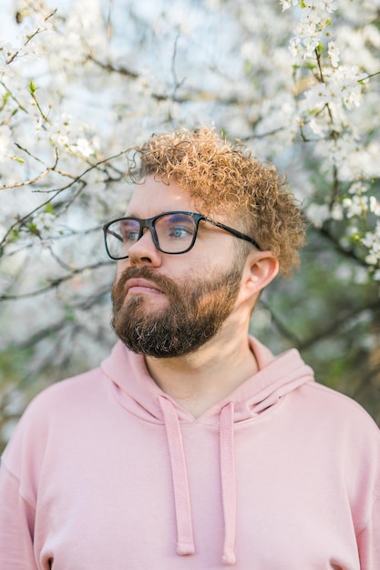 Foto hombre con barba y bigote en la cara sonriente cerca de las flores de sakura o el árbol de primavera en flor suave y