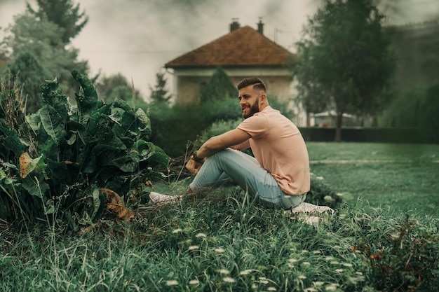 Hombre con barba y camisa rosa posando en un parque verde.