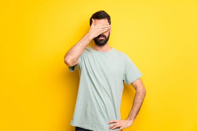 Hombre con barba y camisa verde que cubre los ojos con las manos. No quiero ver algo