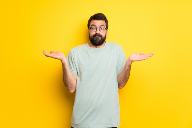 Hombre con barba y camisa verde que tiene dudas al levantar manos y hombros.