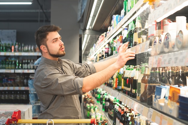 Hombre con barba y camiseta compra una cerveza en el departamento de alcohol de un supermercado.