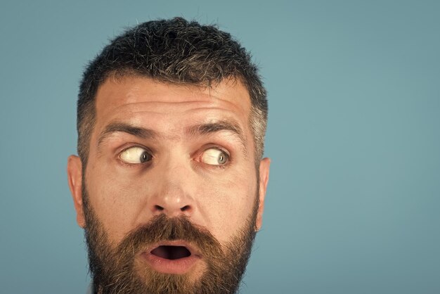 Hombre con barba en la cara asustada sobre fondo azul.