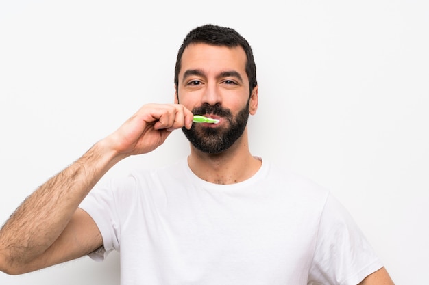 Hombre con barba cepillarse los dientes sobre la pared blanca aislada