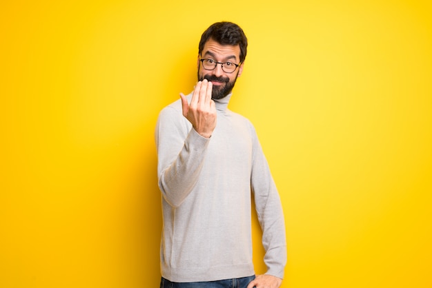 Hombre con barba y cuello alto que invita a venir con la mano. Feliz de que hayas venido