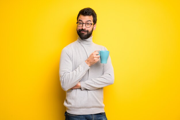 Hombre con barba y cuello alto sosteniendo una taza de café caliente