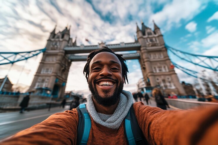Un hombre con barba disfruta tomando una selfie junto al Tower Bridge en Londres con cielos brillantes
