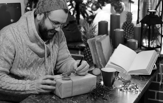 Hombre de barba escribiendo regalos de Navidad sobre una mesa con libros antiguos