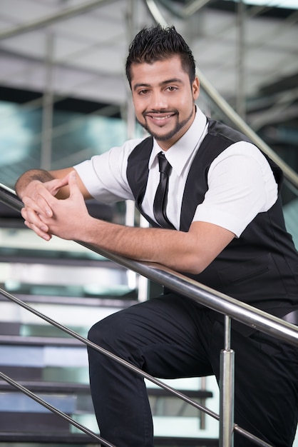 Un hombre con barba está parado en los escalones y sonriendo.